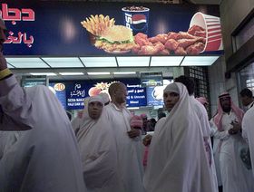 متسوقون أمام فرع لدجاج كنتاكي التابع لشركة أمريكانا في مكة. السعودية - المصدر: غيتي إيمجز