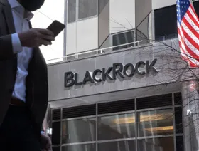 أحد المشاة يحمل هاتفاً ذكياً يعبر من أمام المقر الرئيسي لشركة بلاك روك. في نيويورك، الولايات المتحدة - المصدر: بلومبرغ