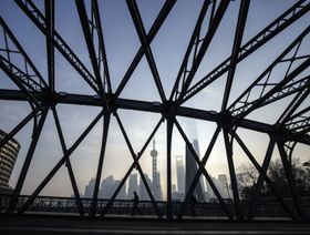 أحد المارة يمشي على جسر يمر قبالة مباني في منطقة لوجياتسوي المالية بحي بودونغ في مدينة شنغهاي الصينية - المصدر: بلومبرغ