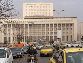 صورة من وسط العاصمة السورية دمشق تظهر سيارات وفي الخلف مقر مصرف سورية المركزي وعليه العلم الجديد للبلاد - بلومبرغ