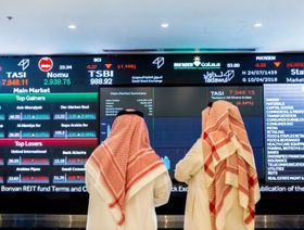شخصان ينظران إلى شاشة كبيرة لعرض أسعار تداولات سوق الأسهم السعودية في العاصمة الرياض - المصدر: بلومبرغ