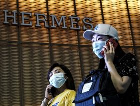 أشخاص يرتدون الكمامات ويمشون بجوار متجر "هيرميس" في ووهان، الصين - المصدر: غيتي إيمجز