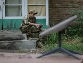 جندي أوكراني ينظر إلى هاتف ويبدو أمامه هوائي استقبال من شركة "ستارلينك" - Getty Images