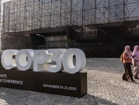 سيدتان تمران بجوار لافتة تحمل شعار "كوب 30" خارج متنزه "باركي دا سيدادي"، المقر الرئيسي لانعقاد القمة في مدينة بيليم بولاية بارا البرازيلية - بلومبرغ