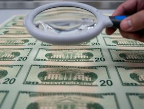 شخص يحمل عدسة مكبرة فوق مجموعة من الأوراق النقدية من فئة 20 دولاراً في واشنطن العاصمة، الولايات المتحدة  - المصدر: بلومبرغ