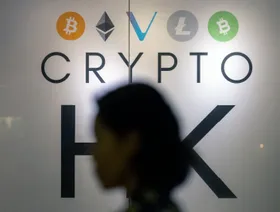 سيدة تعبر من أمام لوحة تعرض شعارات لعملات رقمية مختلفة، هونغ كونغ، الصين - المصدر: بلومبرغ