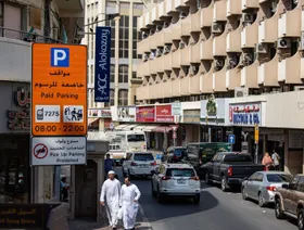 مارة وسيارات بجانب لوحة تحمل تعليمات لمواقف السيارات بأحد الشوارع الجانبية في دبي - المصدر: بلومبرغ