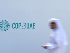 شخص يمر أمام جدار يزينه شعار قمة المناخ "كوب 28"في دبي، الإمارات العربية المتحدة - المصدر: غيتي إيمجز