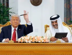 الرئيس الأميركي دونالد ترمب يلوح بقلمه وأمير قطر الشيخ تميم بن حمد آل ثاني يبتسم وبين يديه وثائق الاتفاقية التي تم التوقيع عليها بين الجانبين - رويترز 