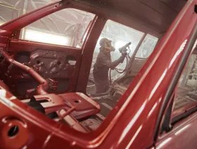 عامل في مصنع سيارات يعمل على طلاء هيكل سيارة باللون الأحمر باستخدام مسدس رش الدهانات - بلومبرغ