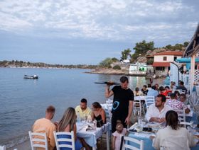 نادل يخدم زبائن في مطعم بجانب البحر في هالكيديكي، اليونان - بلومبرغ