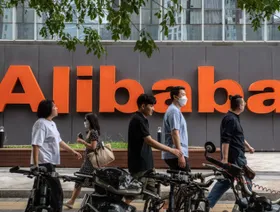 أشخاص يمرون أمام شعار شركة "علي بابا" على واجهة مقرها في بكين، الصين - بلومبرغ