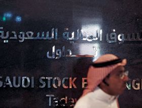 رجل يعبر من أمام جدار تزين بشعار السوق المالية السعودية "تداول"، داخل مقر البورصة في العاصمة السعودية الرياض (15 يونيو 2015) - المصدر: بلومبرغ
