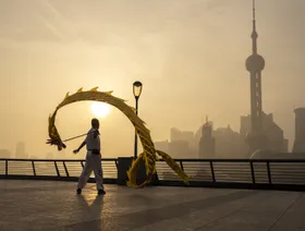 أحد المشاة مع طائرة ورقية على شكل تنين على طول السور أمام المباني في منطقة "لوجيازوي" المالية في بودونغ في شنغهاي، الصين - المصدر: بلومبرغ