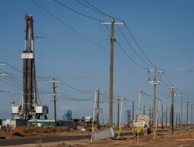 أعمدة توصيل كهرباء خلفها منصة حفر نفطية في حوض برميان بولاية تكساس، الولايات المتحدة الأميركية - بلومبرغ