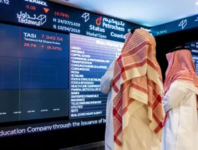 شخصان يطلعان بيانات أسعار الأسهم على لوحة معلومات إلكترونية في سوق الأسهم السعودية 'تداول' - صورة أرشيفية - المصدر: بلومبرغ