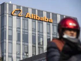 رجل يقود دراجة نارية يعبر بالقرب من مبنى يحمل العلامة التجارية لمجموعة علي بابا الصينية - المصدر: بلومبرغ