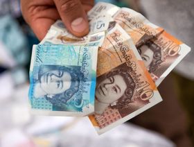 بائع يحمل أوراق نقدية من فئة عشرة وخمسة جنيهات إسترليني في أحد المحلات بمنطقة باركينج، المملكة المتحدة - المصدر: بلومبرغ
