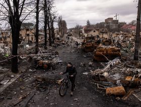رجل يدفع دراجته وسط حطام سيارات حربية مدمرة في منطقة بوشا، شمال غرب كييف، بأوكرانيا، بتاريخ 6 أبريل 2022 - المصدر: بلومبرغ