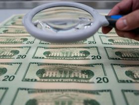 شخص يحمل عدسة مكبرة فوق مجموعة من الأوراق النقدية من فئة 20 دولاراً في واشنطن العاصمة، الولايات المتحدة - المصدر: بلومبرغ
