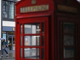 أحد المشاة وراء صندوق هاتف أحمر اللون أثناء مرورها أمام متجر "إي إي" للهواتف المحمولة، تديره "أورانج" و"دويتشه تيليكوم" في لندن، المملكة المتحدة  