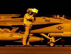 أحد أفراد طاقم مدرج الطيران يشير إلى مقاتلة من طراز " F/A-18" سوبر هورنيت أثناء إقلاعها من حاملة الطائرات يو إس إس دوايت دي أيزنهاور جنوب البحر الأحمر، في 19 مارس. - المصدر: بلومبرغ