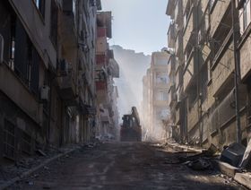 حفار يسير على طول شارع تصطف على جانبيه المباني السكنية المتضررة من الزلازل في هاتاي، تركيا - المصدر: بلومبرغ