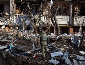 جندي أوكراني يتفقد أنقاض مبنى سكني مدمر في كييف في 15 مارس 2022. رغم الهدوء النسبي للأسواق، ما زالت الحرب الأوركرانية تمثل تهديداً كبيراً للاقتصاد العالمي - المصدر: أ.ف.ب