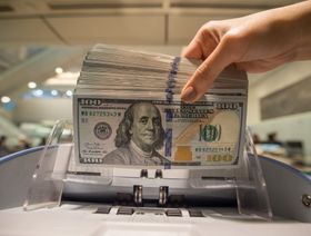 موظف يستخدم آلة لحساب الأوراق النقدية من فئة مائة دولار أميركي - المصدر: بلومبرغ