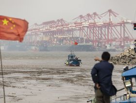 رجل يقف على ظهر مركب ويشير بيده إلى سفن راسية في ميناء لمناولة الحاويات في الصين - المصدر: بلومبرغ