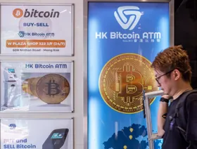 شخص يعبر من أمام لوحة إعلانية لجهاز صراف آلي يحمل شعار "بتكوين" في هونغ كونغ - بلومبرغ