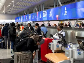 مسافرون يباشرون إجراءات السفر وحقائبهم أمام موظفي شركة طيران بأحد المطارات - بلومبرغ
