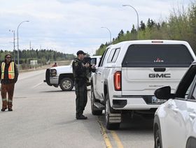 مجموعة ضباط أمن يخلون السكان ويأمرون السيارات بالابتعاد عن المناطق المتضررة من حرائق الغابات في كندا - المصدر: بلومبرغ