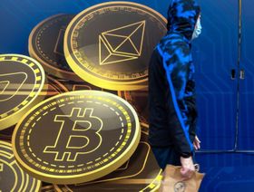 شخص يرتدي كمامة يعبر من أمام لوحة إعلانية تحمل شعارات عملتي "بتكوين" و"إيثريوم" المشفرتين - المصدر: بلومبرغ