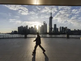 رجل يسير على طول منطقة البوند أثناء شروق الشمس، وخلفه تبرز مباني منطقة لوجيازوي المالية في شنغهاي، الصين - بلومبرغ