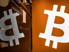 شعار بتكوين على لافتة منعكساً على واجهة زجاجية - بلومبرغ