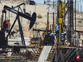 عمال يرتدون الزي الأزرق يعملون في حقل نفط قرب بيكرسفيلد بولاية كاليفورنيا، وسط معدات الحفر ووحدات الضخ - Getty Images