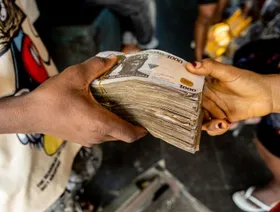أحد العملاء يسلم حزماً من أوراق نقدية فئة 1000 نيرة لتاجر داخل سوق بمدينة لاغوس في نيجيريا. الجمعة 22 أبريل 2022 - المصدر: بلومبرغ