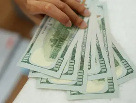 رجل يمسك بأوراق نقدية من فئة مئة دولار أميركي - المصدر: بلومبرغ