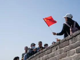 علم الصين يرفرف بيد زائرة لسور الصين العظيم بينما يلتقط لها أصدقاؤها صورة تذكارية - المصدر: بلومبرغ