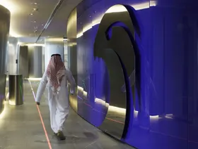 موظف يمر من أمام جدار مثبت عليه شعار شركة بترول أبوظبي الوطنية (أدنوك) بمقر الشركة في أبوظبي، الإمارات العربية المتحدة - المصدر: بلومبرغ