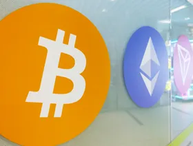شعارات العملات المشفرة "بتكوين" و"إيثر" و"ترون" مُعلقة على واجهة زجاجية لأحد المتاجر - بلومبرغ