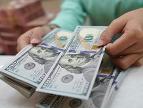 موظفة تقوم بعد أوراق نقدية من فئة 100 دولار أميركي - بلومبرغ