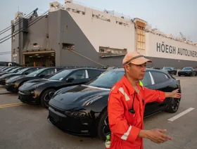 عامل في الميناء وخلفه سيارات كهربائية مخصصة للتصدير في ميناء تايكانغ، الصين - بلومبرغ