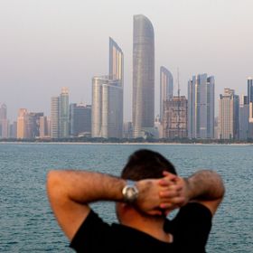 شخص ينظر إلى أفق مدينة أبوظبي من ضفة كورنيش المدينة، وتظهر في العمق أبراج الأعمال في العاصمة الإماراتية. أبوظبي، الإمارات العربية المتحدة. - المصدر: بلومبرغ