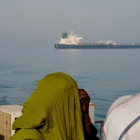 امرأة على قارب يحمل علم إيران تنظر إلى ناقلة نفط في مضيق هرمز - بلومبرغ