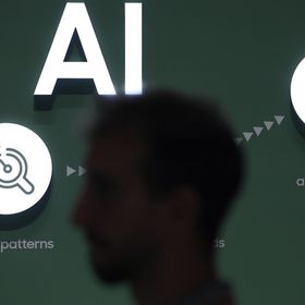 شخص يعبر من أمام لوحة تشرح بعض المعلومات عن الذكاء الاصطناعي - المصدر: بلومبرغ