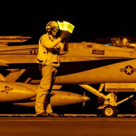 أحد أفراد طاقم الإقلاع يوجه إشارات مضيئة بيديه لطائرة مقاتلة من طراز " F/A-18" سوبر هورنيت قبل إقلاعها من حاملة الطائرات يو إس إس دوايت دي أيزنهاور جنوب البحر الأحمر، في 19 مارس 2025 - المصدر: بلومبرغ