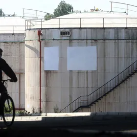 رجل يقود دراجته الهوائية بالقرب من خزانات نفط في منشأة تديرها شركة "غازبروم نفط" في العاصمة الصربية بلغراد - المصدر: بلومبرغ