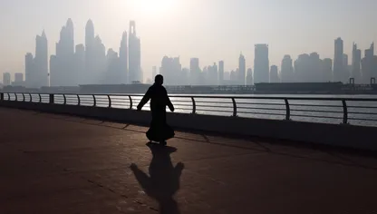 امرأة تسير على ممشى في دبي مع أفق ناطحات السحاب في الخلفية - بلومبرغ